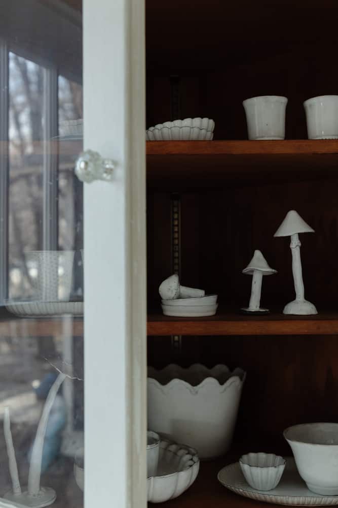 Opened glass bookcase door with wood shelves filled with white french pottery pieces.